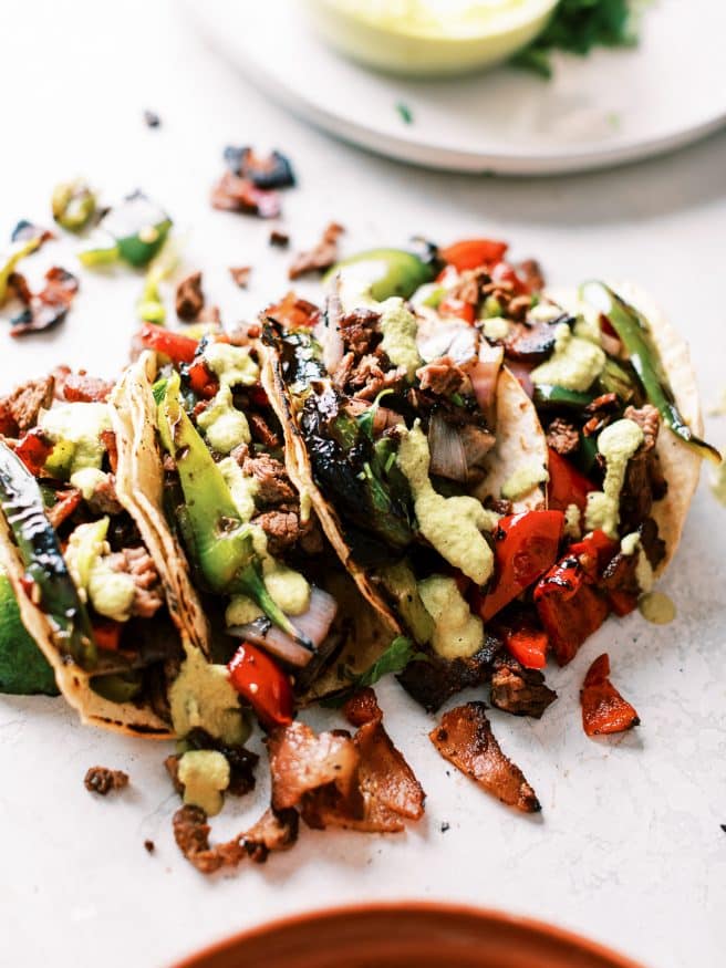 Alambre tacos are Carne Asada topped with bacon, and grilled onions and peppers, topped with a roasted pepper and green sauce and stuffed into a taco. Do I have your attention yet?